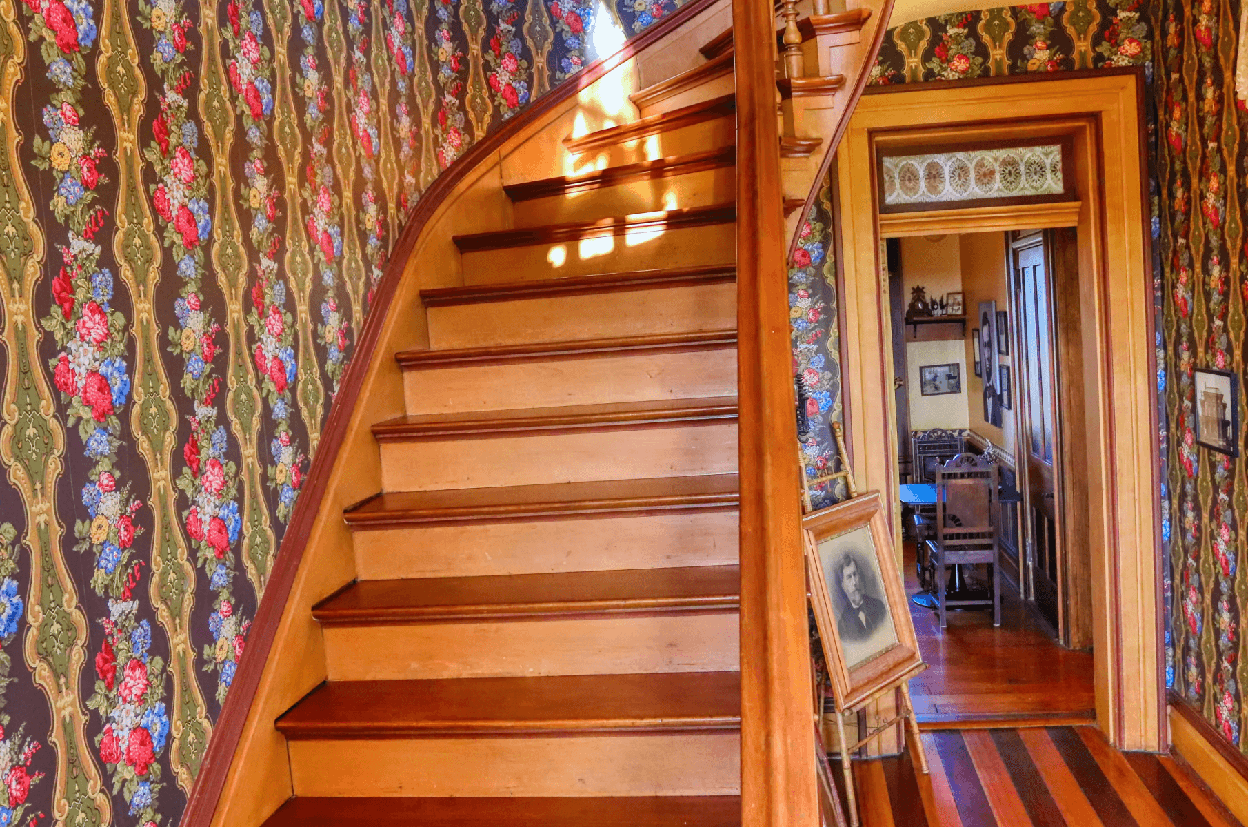 John Vorhees portrait and story and the Elegant wooden staircase in a vintage home with patterned wallpaper and lace curtain.