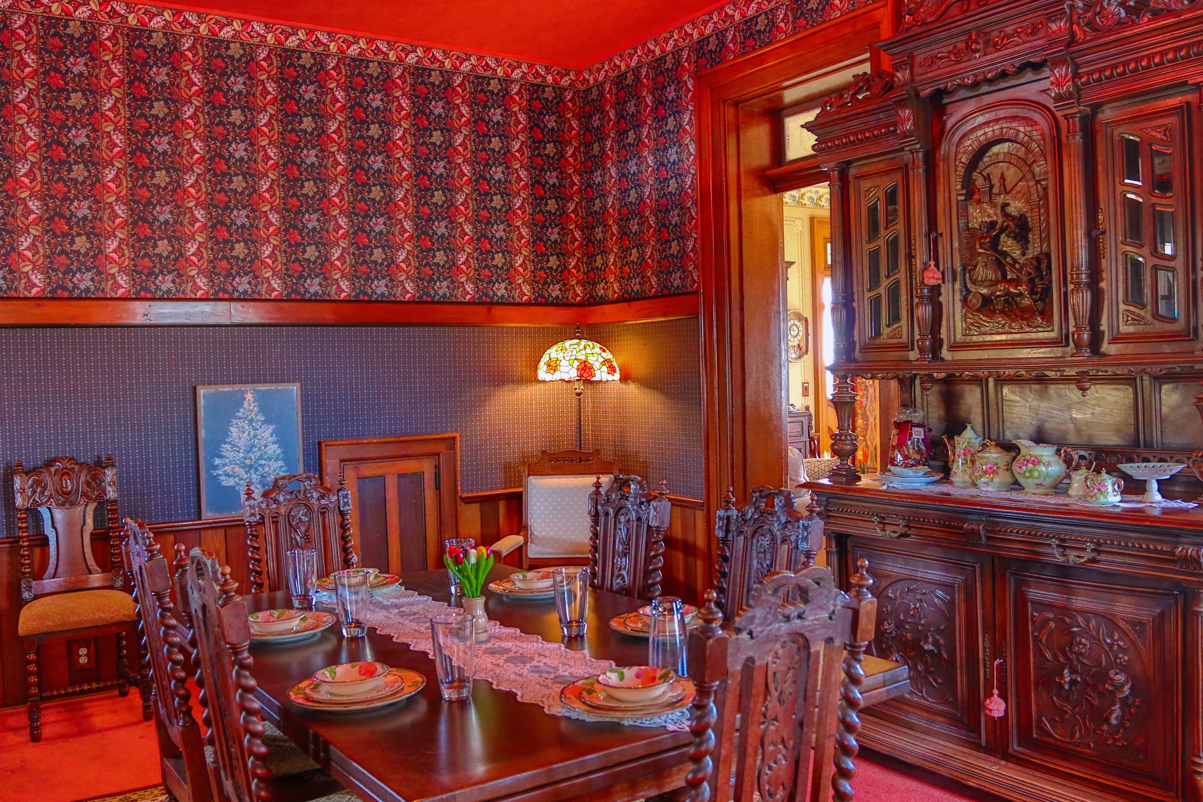 A richly decorated dining room featuring ornate wooden furniture, a vintage hutch, and a warm color scheme.