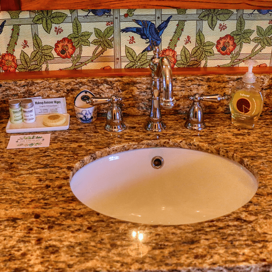 A bathroom sink with a granite countertop, decorative wallpaper, and various toiletries.