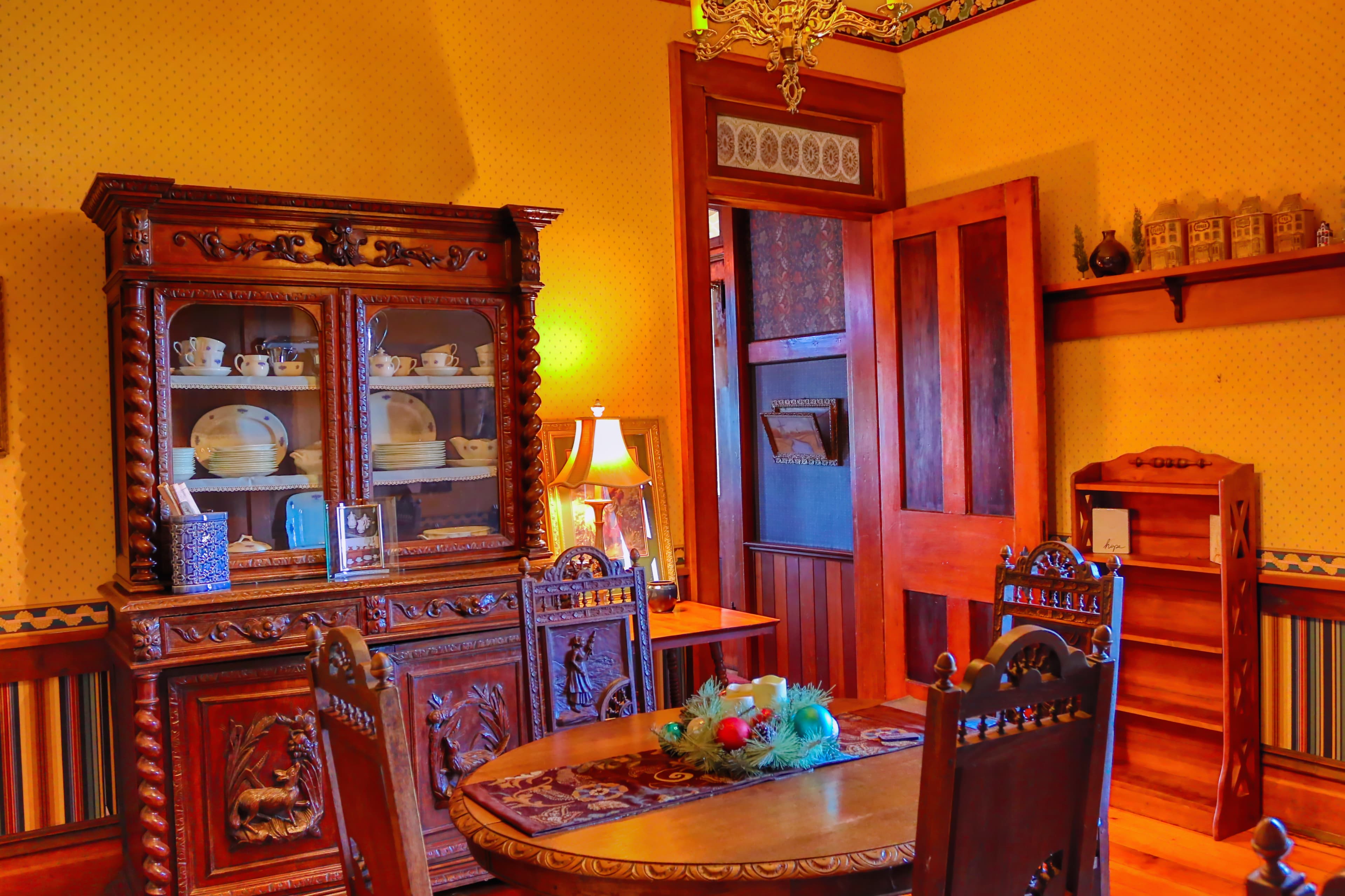 A vintage dining room featuring ornate wooden furniture, a china cabinet, and warm ambient lighting.