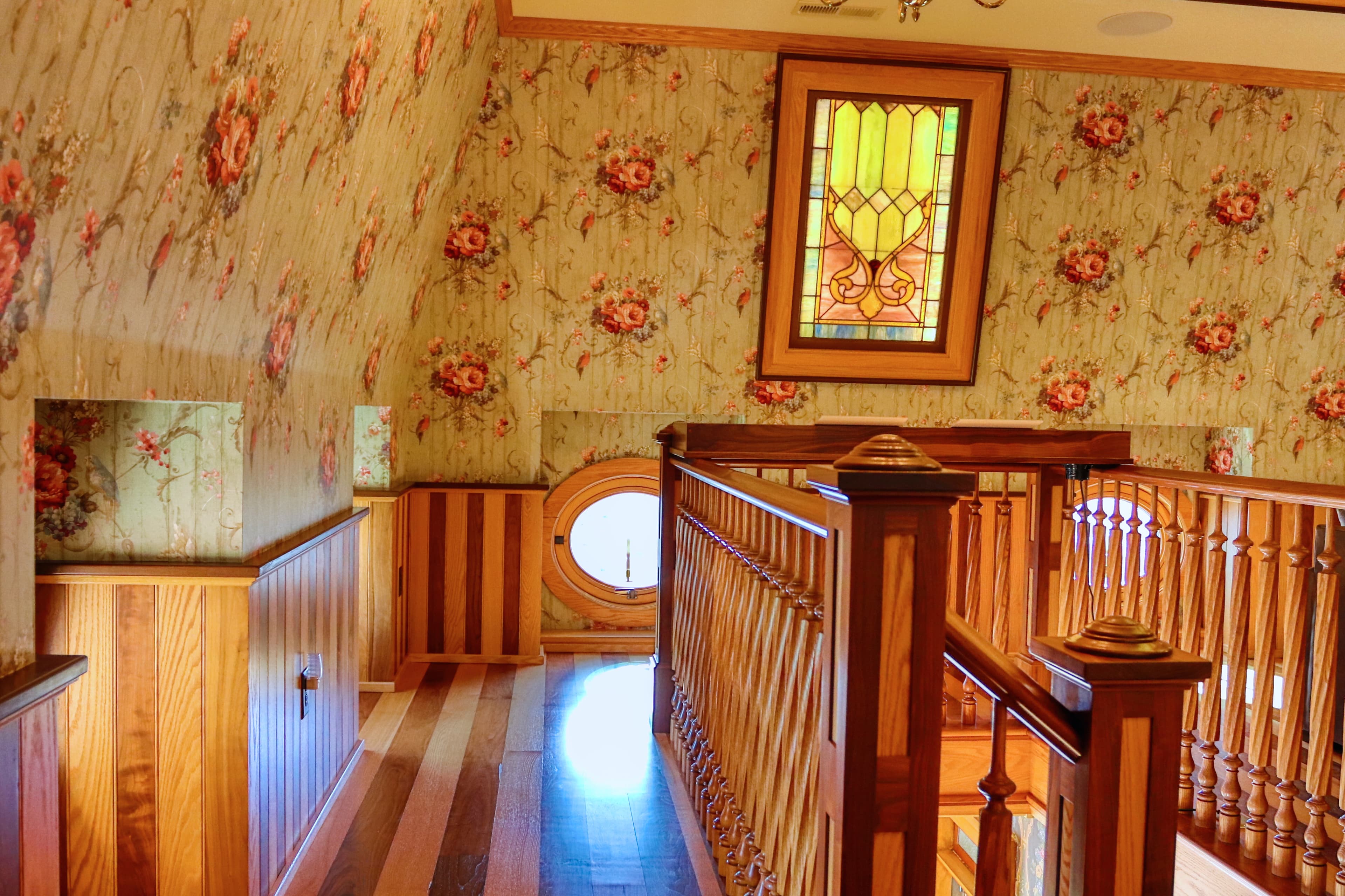 A bright staircase featuring floral wallpaper and a stained glass window.