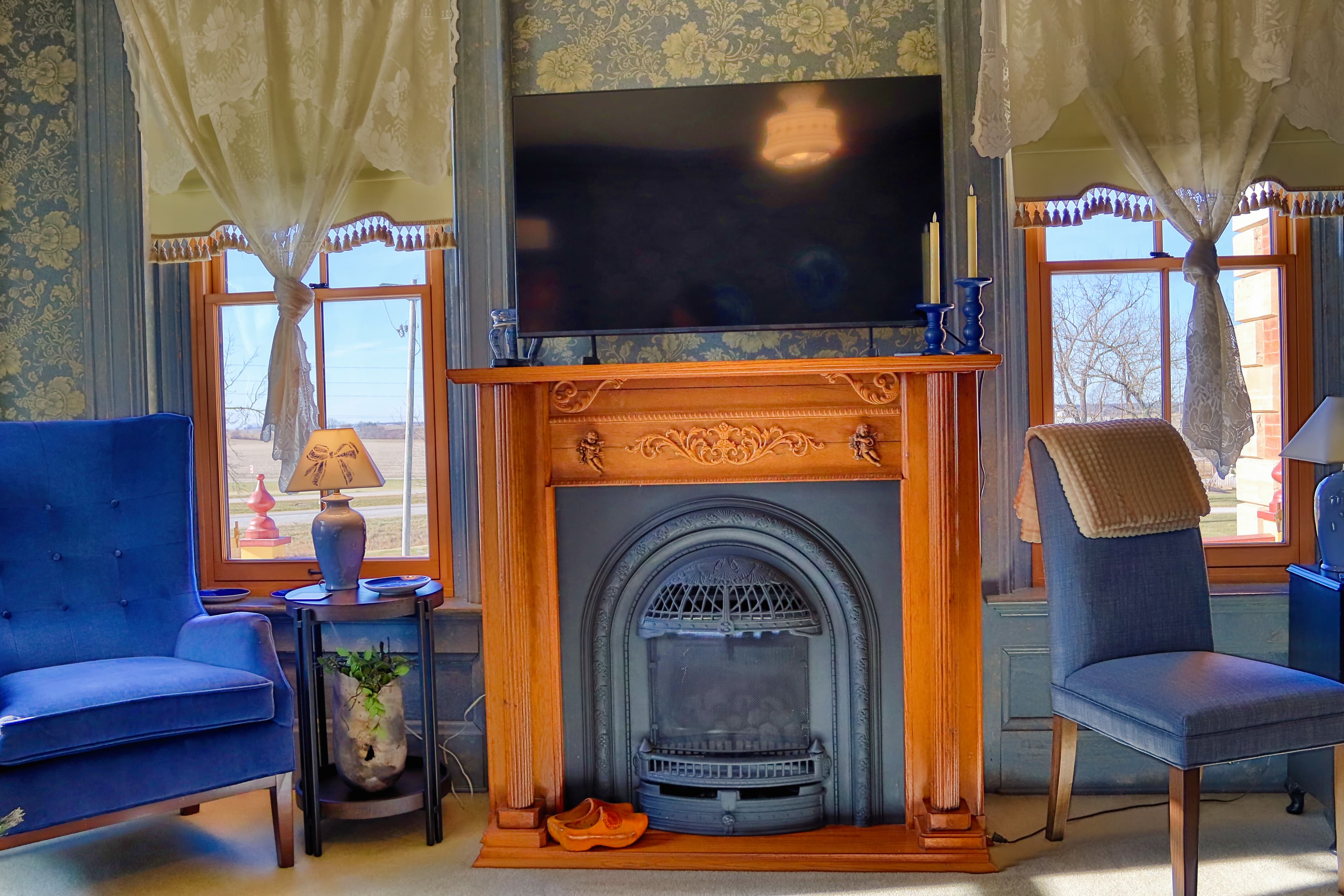 Cozy living room with a blue armchair, wooden fireplace, and a flat-screen TV above.
