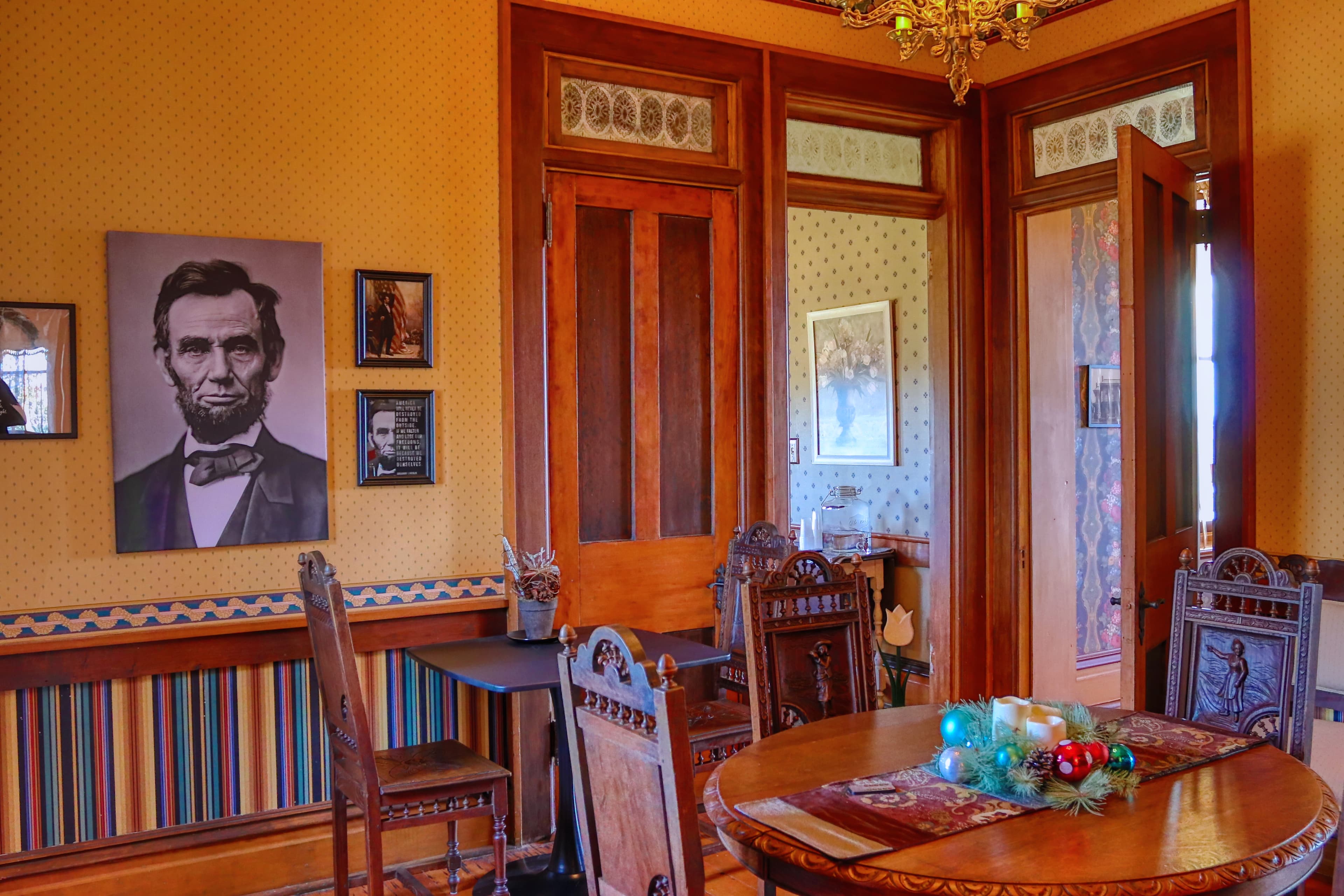Interior of a historically styled room featuring a portrait of Abraham Lincoln, a wooden table, and decorative chairs.