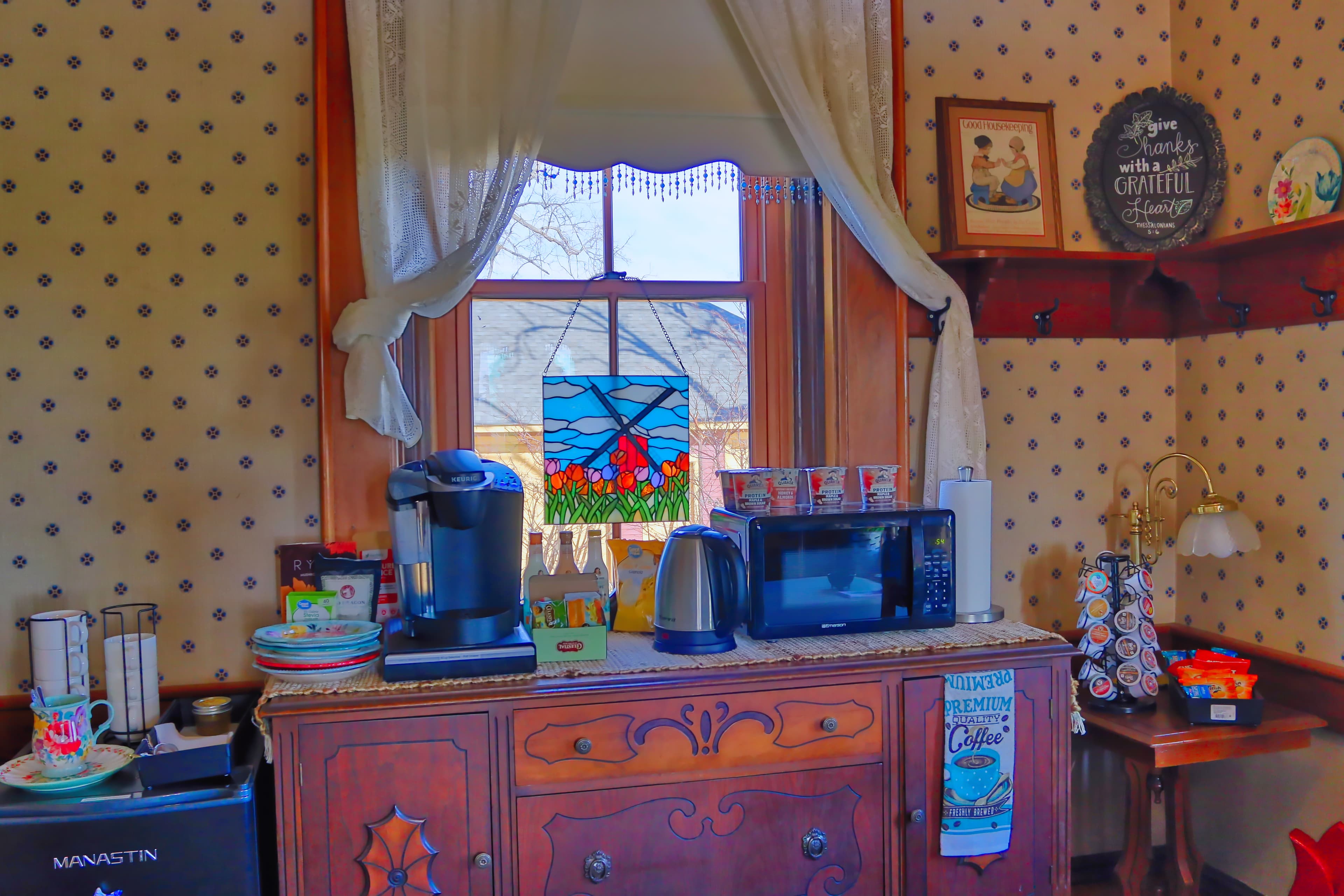 A cozy kitchen nook featuring a stained glass window, coffee maker, microwave, and decorative accents.