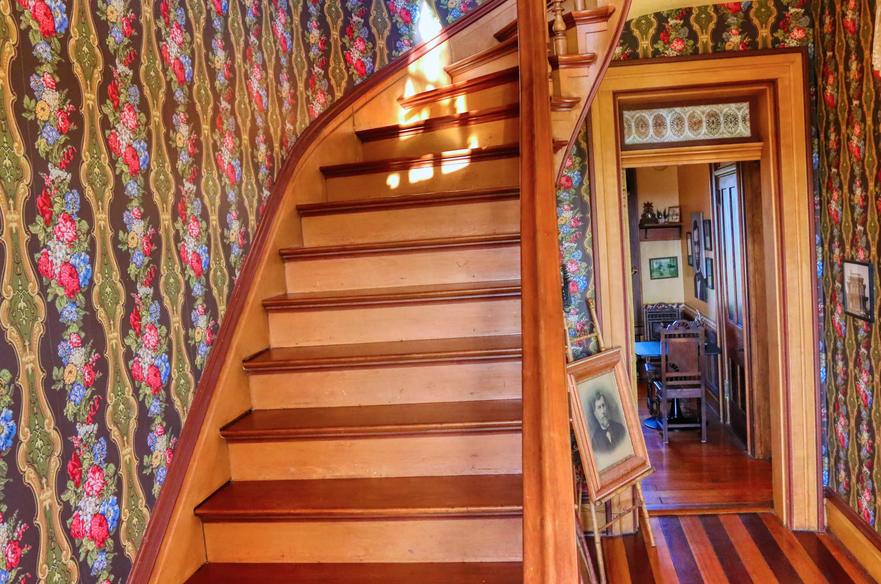 John Vorhees portrait and story and the Elegant wooden staircase in a vintage home with patterned wallpaper and lace curtain.