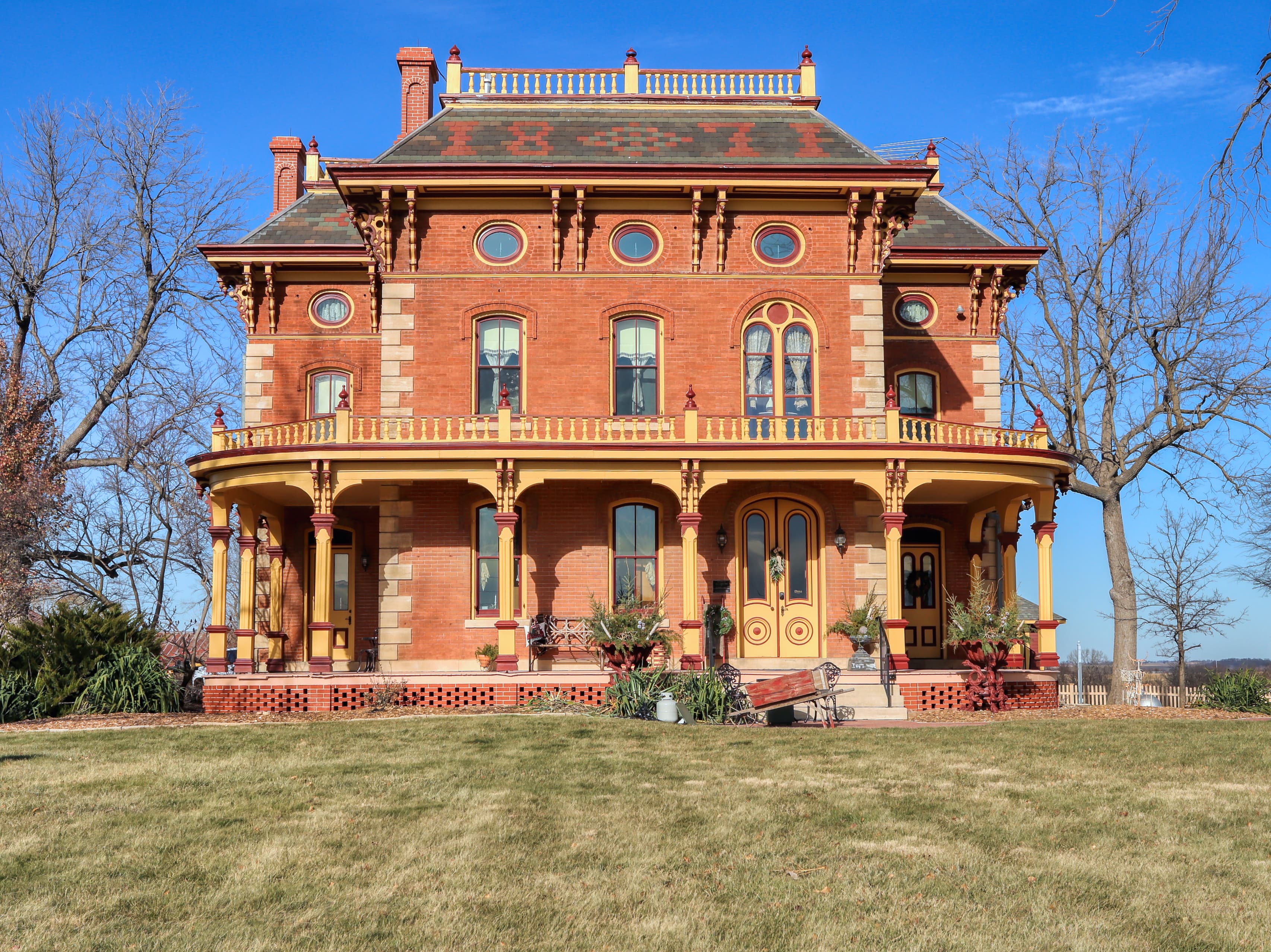 Victorian-style red brick house with a wraparound porch and lush garden.
